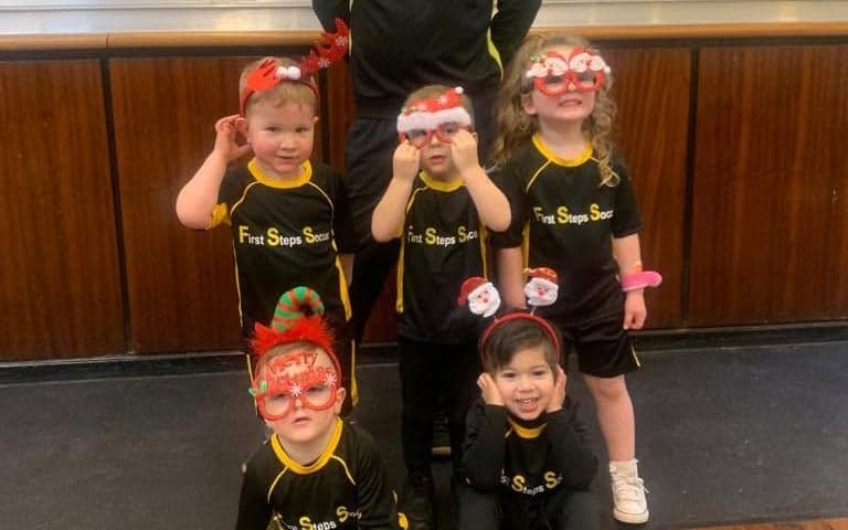 Young First Steps Soccer players in festive glasses with their coach