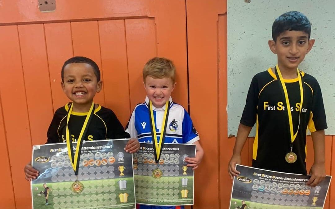 Three young First Steps Soccer players with their medals and attendance charts